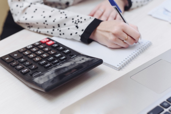 image of a cropped woman writing on notebook with calculator beside her depicting HVAC load calculation