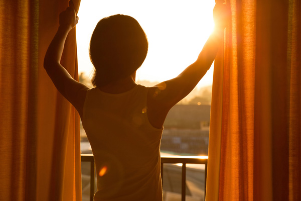 homeowner closing curtains to block heat and sunlight