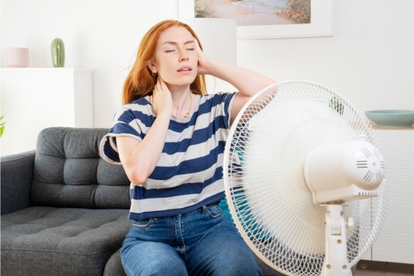 woman staying cool in front of fan as temporary solution to air conditioner failure