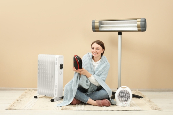 woman with different space heaters while wearing a blanket