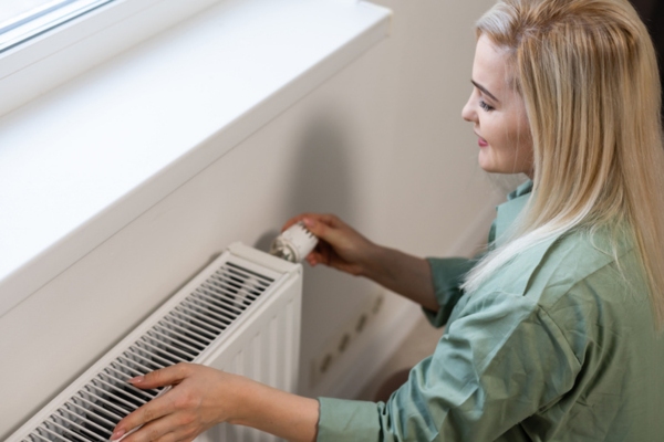 image of a woman turning on heating radiator at home