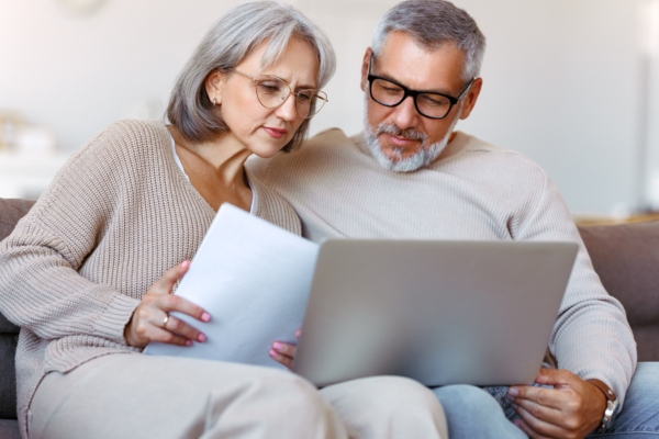 couple thinking while looking at laptop & documents depicting deciding between will-call or automatic oil delivery